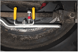 The image displays a brake stroke indicator tool in use, mounted within the wheel area of a vehicle to measure the stroke of the brake chamber. This tool includes a red marker and a caliper-style gauge with yellow handles, set against the backdrop of a brake drum, illustrating the real-world application and importance of precise brake measurement for safety.